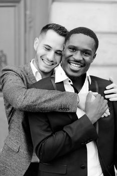 Black and white portrait of two hugging boys, caucasian and afro american, wearing suits. Concept of gays and lgbt.