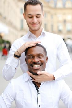 Caucasian boy holding afro american guy head by hands, wearing white shirt. Concept of stylish boy and haircut.
