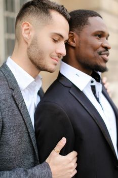 Caucasian man hugging afro american boy, wearing suit. Concept of relationship and same sex couple.