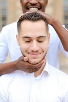 Portrait of caucasian man, afro american guy holding boy head by hands.