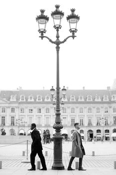 Black and white photo of afro american and caucasian boys standing near street lantern, wearing suits. Concept of urban photo session and life style.