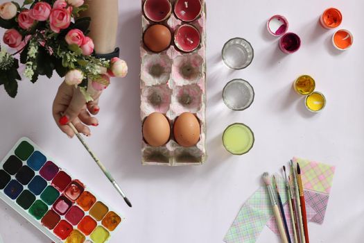 painting eggs for Easter, eggs, paints, brushes, flowers lie on a pink background