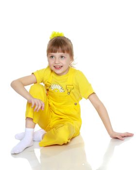 Girl with a short bangs on her head and bright yellow overalls.She crouched down on the white advertising banner.