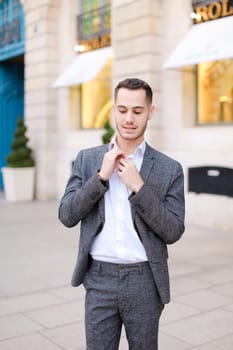 Young cacuasian handsome male person wearing suit standing near building outdoors. Concept of fashion and businessman, urban life.