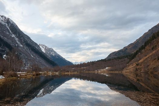 autumn landscape, lake in the mountains, water surface, fallen trees, coniferous forest and the first snow, mountains on the background