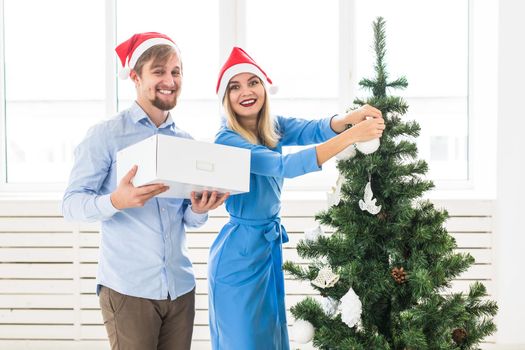 Holidays and festive concept - Young family couple decorating the christmas tree.