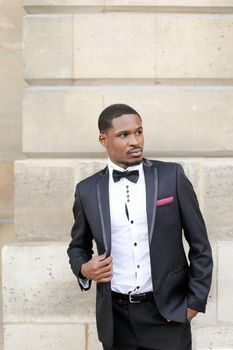 Afro american happy successful man wearing dark suit and standing outside in wall background. Concept of black businessman.