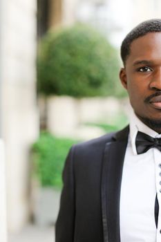 Portrait of afro american happy man wearing dark suit and standing outdoors. Concept of black businessman.