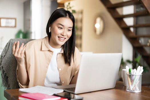 Smiling asian girl talking on laptop, video chatting with friends or students. Young woman tutoring online, teaching lesson via e-learning website.