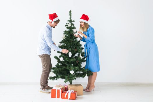 Holidays and festive concept - Young family couple decorating the christmas tree.