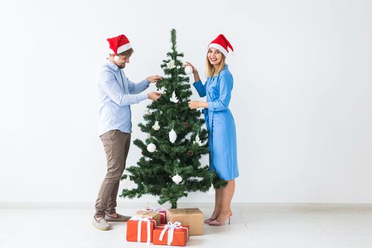 Holidays and festive concept - Young family couple decorating the christmas tree.