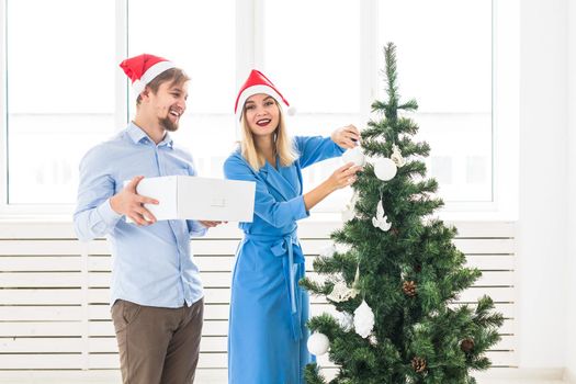 Holidays and festive concept - Young family couple decorating the christmas tree.