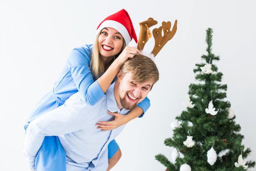 Funny man giving piggyback to his wife while they wearing Santa hats for Christmas holidays at home