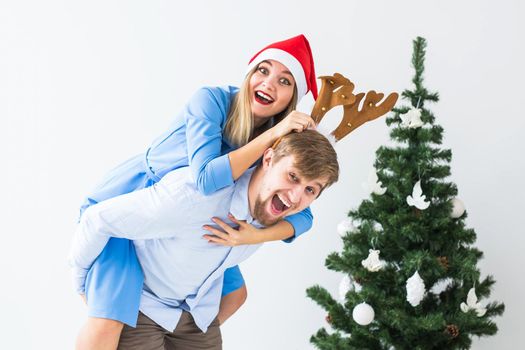 Funny man giving piggyback to his wife while they wearing Santa hats for Christmas holidays at home