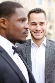 Focus on caucasian man wearing suit standing near afro american guy. Concept of business and male fashion.