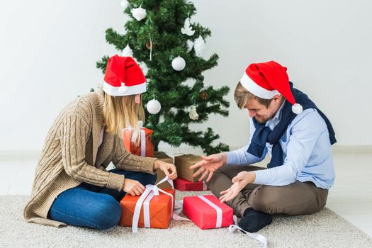Christmas and holidays concept - Young happy couple wearing santa hats opening gifts at home