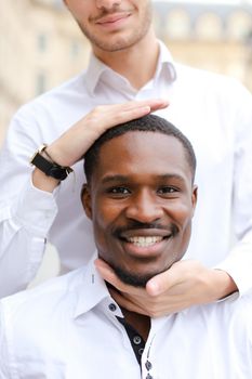 Caucasian man holding afro american guy head by hands.