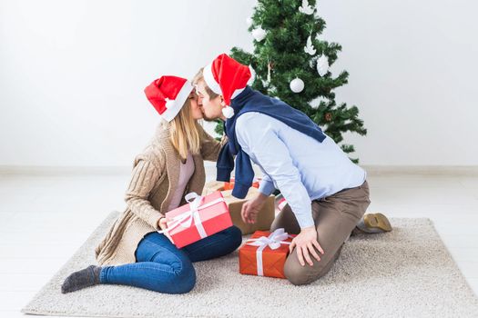 Christmas and holidays concept - Young happy couple wearing santa hats opening gifts at home