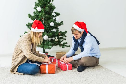 Christmas and holidays concept - Young happy couple wearing santa hats opening gifts at home