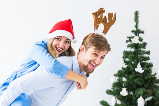 Funny man giving piggyback to his wife while they wearing Santa hats for Christmas holidays at home