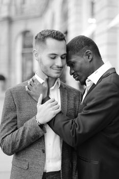 Black and white photo of afro american gay hugging caucasian boy outside, wearing suits. Concept of lgbt and same sex couple.