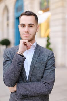 Portrait of young cacuasian handsome male person wearing suit standing near building outdoors. Concept of fashion and businessman, urban life.