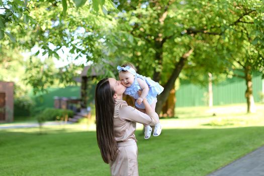 Young mother holding little female child in garden. Concept of motherhood and resting on nature.