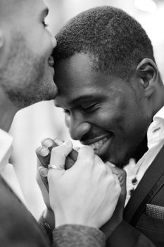 Balck and white photo of caucasian man kissing afro american boy forehead and holding hands. Concept of lgbt and same sex couple.