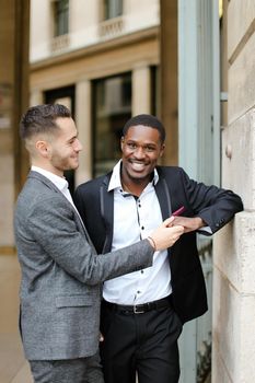 Caucasian man hugging handsome afro american guy outside and wearing suit. Concept of happy same sex couple and gays.