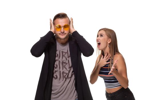 Young family couple have conflict. Angry blonde young European woman gestures with hands, shouts at husband who is guilty, stands together against white background, have dispute and quarrel