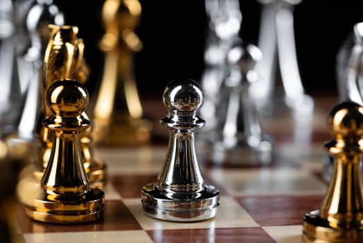 Gold and silver chess figures placed on wooden chessboard. Intellectual duel and tactical battle in business. Strategy planning, leadership and teamwork concept. Close-up metal chess pieces on board.