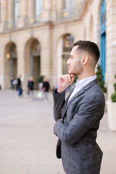 Young american boy wearing grey suit standing near building. Concept of male fashion and successful businessman.