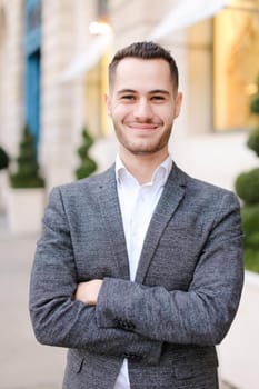 Portrait of happy young caucasian man wearing grey suit outside. Concept of successful businessman and male fashion.