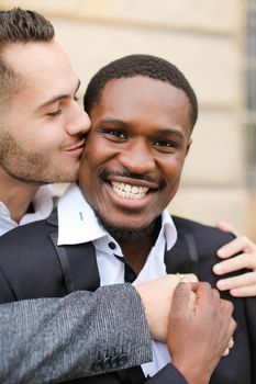 Portrait of caucasian man kissing afroamerican boy. Concept of gays and happy same sex couple.