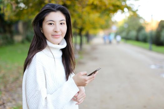 Japanese girl typing by smartphone and walking in park. Concept of asian female person and chinese modern technology.