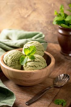 Mint ice cream scoops in wooden bowl on old wooden table background. Homemade summer food concept with copy space.