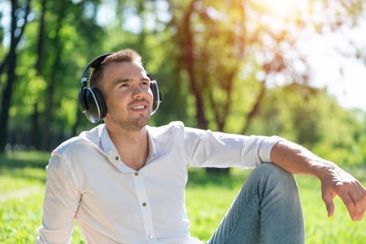 Young man in the park listens to music. He sits on the grass and enjoys music.