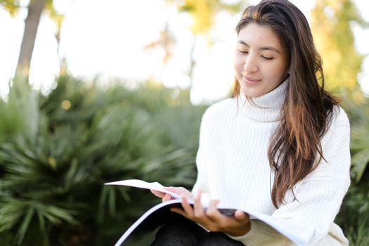 Korean female student sitting on stump in park and reading papers. Concept of preparing before exam and asian woman.