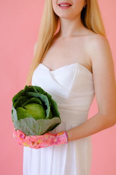 Smiling girl keeping cabbage in pink monophonic background. Concept of harvest and photo session at studio.