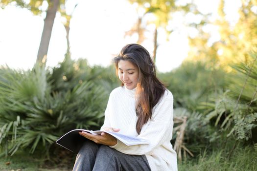 Japanese female student sitting on stump in park and reading papers. Concept of preparing before exam and asian woman.