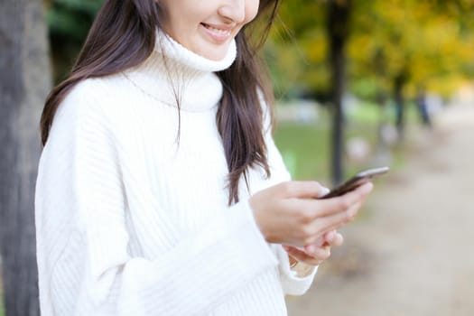 Focus on phone, runette smiling woman walking in park and chatting by smartphone. Concept of modern technology and strolling in park with mobile phone.