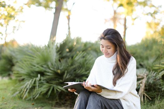 Chinese pretty female student sitting on stump in park and reading papers. Concept of preparing before exam and asian woman.