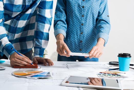 Woman taking photo of technical drawing with smartphone. Designers working with color swatches and construction blueprint at workplace. Interior design, architectural decoration and renovation.