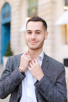 Portrait of young cacuasian male person wearing suit standing near building outdoors. Concept of fashion and businessman, urban life.