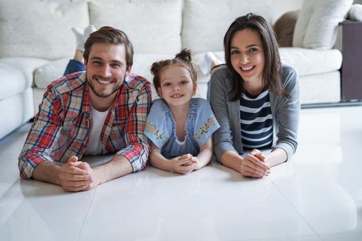 Young caucasian family with small daughter pose relax on floor in living room, smiling little girl kid hug embrace parents, show love and gratitude, rest at home together