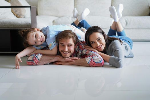 Young caucasian family with small daughter pose relax on floor in living room, smiling little girl kid hug embrace parents, show love and gratitude, rest at home together