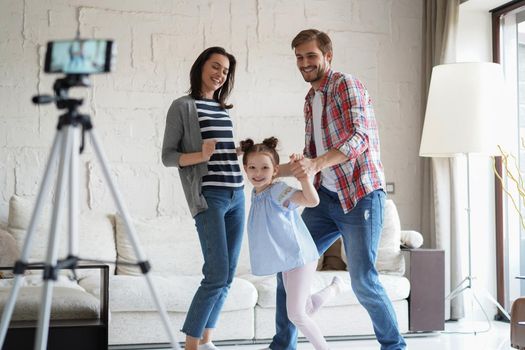 Happy young family dancing at home with his little cute daugther, shooting video