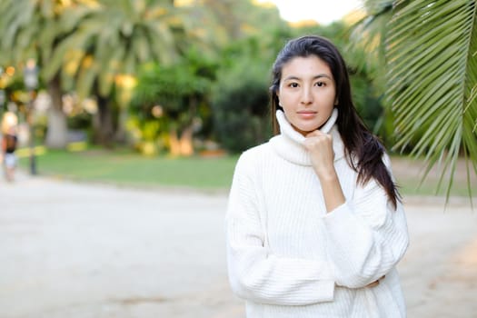 Chinese woman in white sweater standing near palm leaf. Concept of asian beauty and female person on tropical resort.