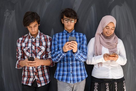 Group of Arab teens taking selfie photos on a smartphone with a black chalkboard in the background. Selective focus. High quality photo