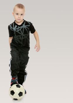 Cute little boy with the ball.The boy demonstrates his strong kick.On a gray background.